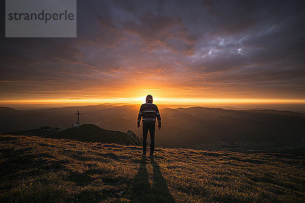 Rückansicht eines Mannes  der bei Sonnenuntergang auf einem Berg steht