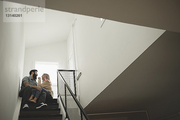 Niedriger Blickwinkel auf ein romantisches Paar  das sich auf einer Treppe zu Hause unterhält