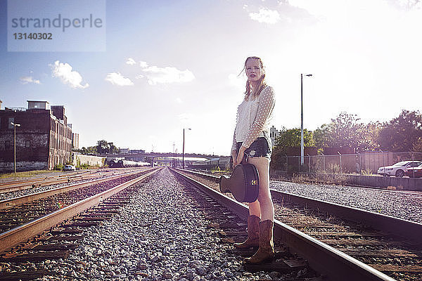 Frau trägt Musikkoffer  während sie auf Eisenbahnschienen steht