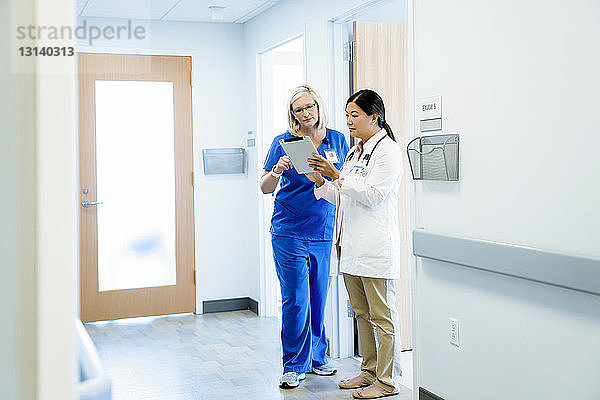 Ärztinnen diskutieren über Tablet-Computer  während sie im Krankenhauskorridor stehen