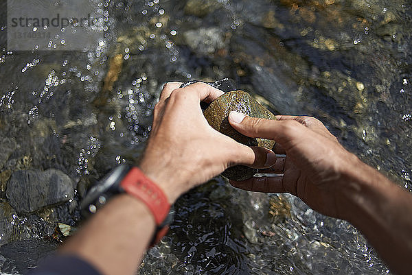 Abgehackte Hände eines Wanderers beim Pflücken von Steinen aus fließendem Fluss