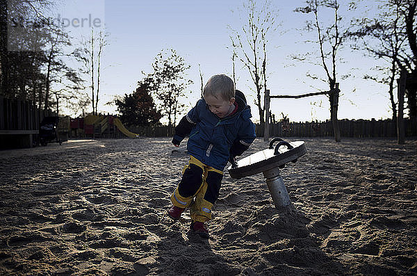 Fröhlicher Junge in voller Länge beim Spielen im Sand auf dem Spielplatz