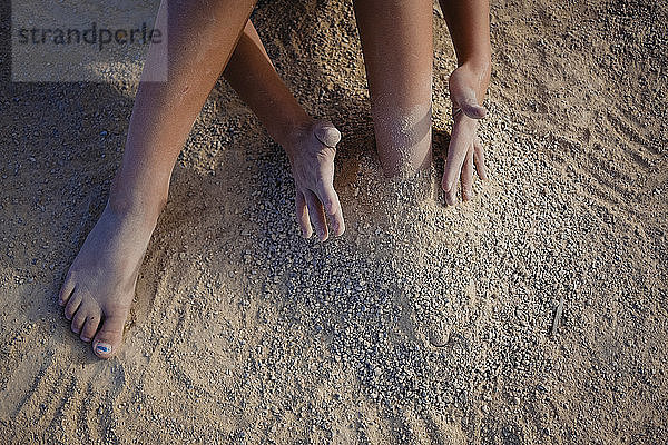 Niedriger Abschnitt eines Mädchens  das am Strand mit Sand spielt