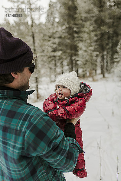 Seitenansicht eines Vaters  der eine niedliche Tochter trägt  während er im Winter im Wald steht