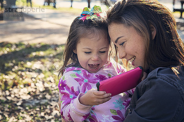 Fröhliche Mutter und Mädchen telefonieren im Park
