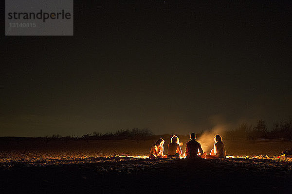 Freunde sitzen nachts am Lagerfeuer am Strand