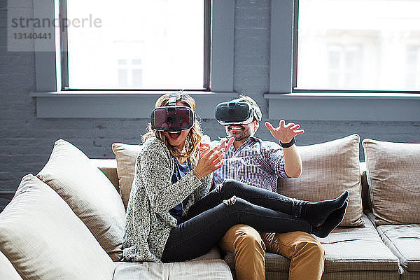 Glückliche Mitarbeiter tragen Virtual-Reality-Simulatoren  während sie im Büro auf dem Sofa sitzen