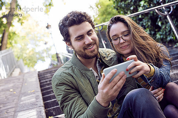Glückliches junges Paar benutzt ein Smartphone  während es auf einer Treppe sitzt