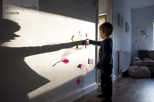 Junge in voller Länge klebt zu Hause Haftnotizen an die Wand