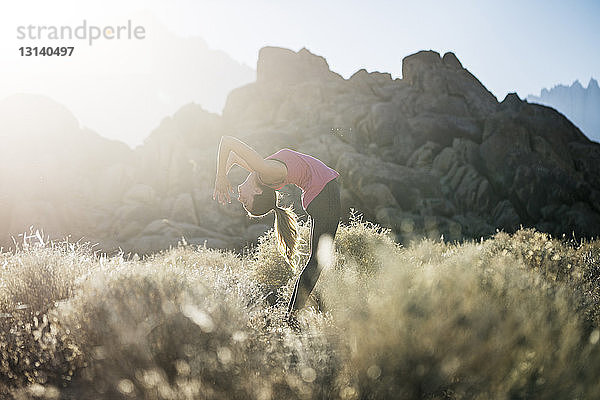 Frau praktiziert bei Sonnenschein Yoga auf Feld gegen Berge