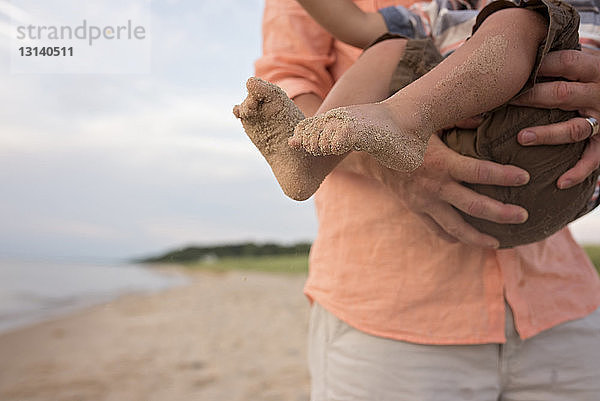 Mittelteil eines Vaters  der seinen Sohn beim Spielen am Strand trägt