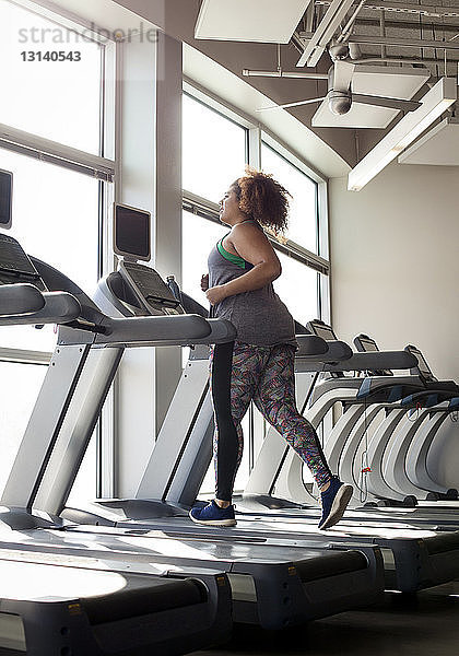 Kurvenreiche Frau läuft in voller Länge auf dem Laufband im Fitnessstudio