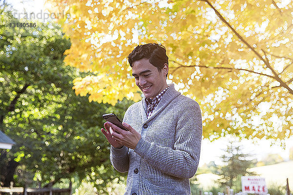 Mann benutzt Mobiltelefon  während er im Herbst an Bäumen steht