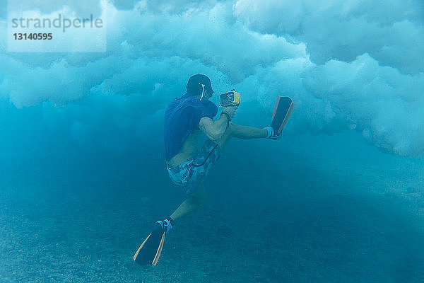 Mann hält Kamera beim Unterwasserschwimmen