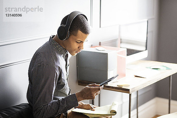 Seitenansicht eines Geschäftsmannes  der Musik hört  während er einen Tablet-Computer im Büro benutzt