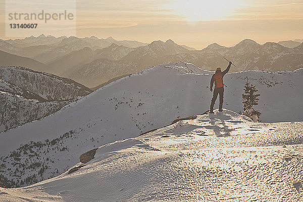 Wandern in voller Länge mit Eispickel auf schneebedeckten Bergen bei Sonnenuntergang