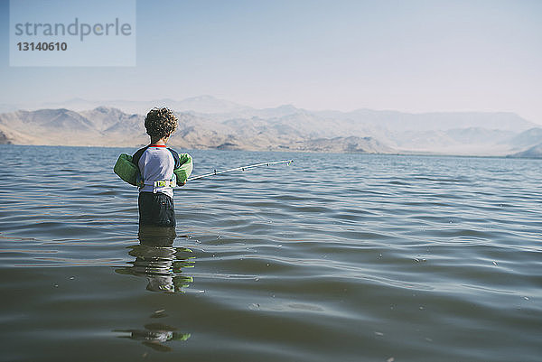 Rückansicht eines Jungen beim Angeln im Fluss vor klarem Himmel während eines sonnigen Tages