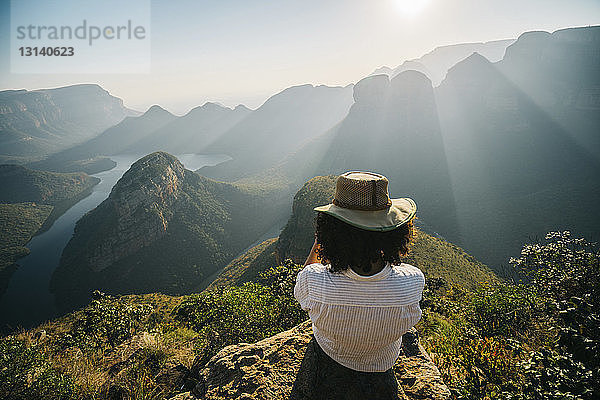 Rückansicht einer Frau mit Hut  die bei sonnigem Wetter auf dem Berg gegen den Himmel schaut