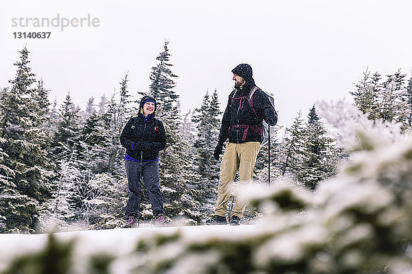 Lächelnde Freunde in voller Länge stehen bei Schneefall im Wald