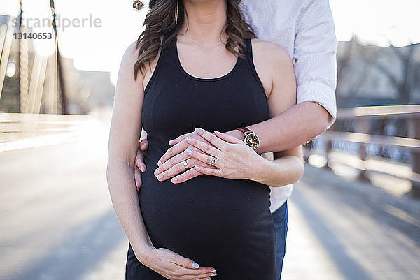 Mittelsektion des Ehemannes  der den Bauch der schwangeren Frau berührt  während er auf der Straße steht