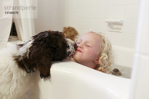 Hund küssendes Mädchen sitzt in Badewanne im Badezimmer