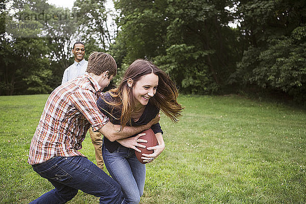 Mann zieht Frau zurück  die den Fussball hält  während ein Freund auf dem Rasen steht