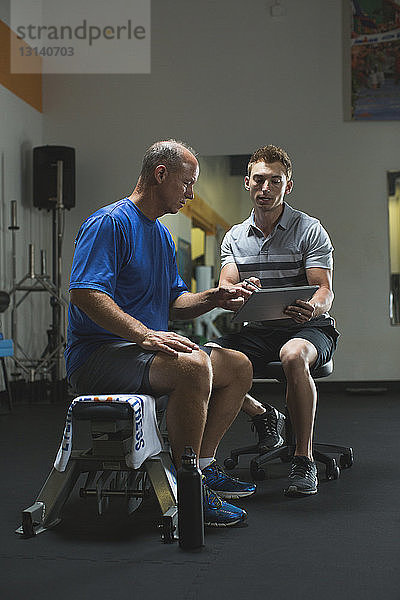 Trainer zeigt dem Kunden einen Tablet-Computer  während er im Fitnessstudio sitzt