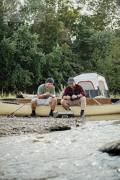 Freunde passen Angelgeräte an  während sie auf dem Boot am See auf dem Campingplatz sitzen