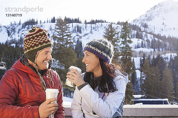 Glückliches Paar trinkt Kaffee  während es vor schneebedeckten Bergen steht