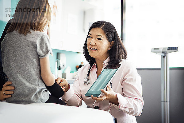 Ärztin zeigt einem Mädchen in der Klinik ein Hand-Röntgenbild am Tablet-Computer