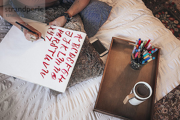 Hochwinkelansicht eines Künstlers  der zu Hause auf dem Bett sitzend Kalligrafie macht