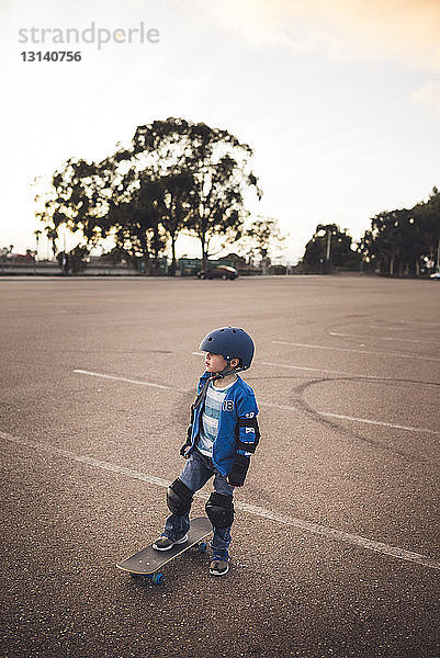 Junge steht mit Skateboard auf dem Feld vor klarem Himmel