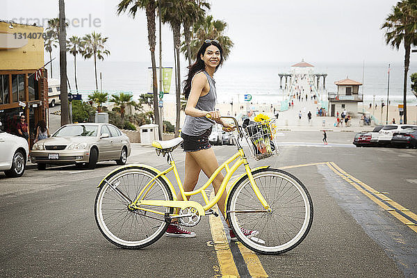 Seitenansicht einer lächelnden Frau mit Fahrrad beim Überqueren der Stadtstraße