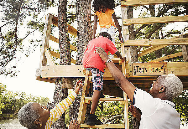 Großeltern helfen Enkel beim Erklimmen der Stufen eines Baumhauses
