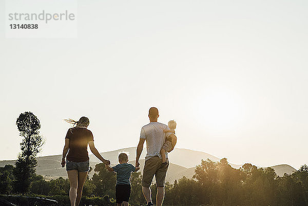 Familie geht bei Sonnenuntergang gegen klaren Himmel auf dem Feld