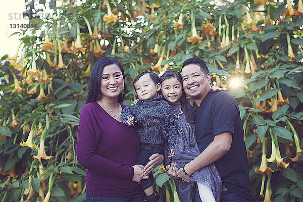 Porträt einer glücklichen Familie gegen blühende Pflanzen im Park