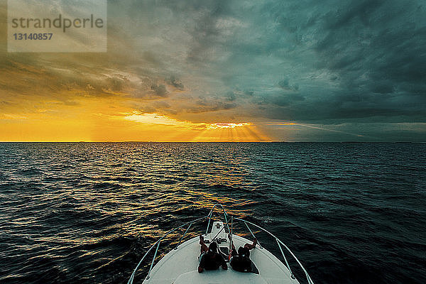 Hochwinkelaufnahme von Männern  die bei Sonnenuntergang auf einer Yacht auf See sitzen