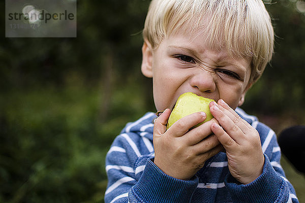 Porträt eines Jungen  der im Hinterhof stehend einen Apfel isst