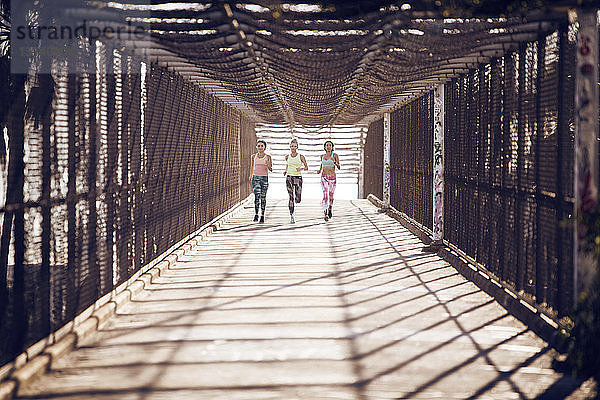 Athletinnen in voller Länge auf überdachter Brücke joggen