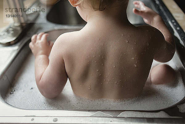 Rückansicht eines im Waschbecken badenden Jungen