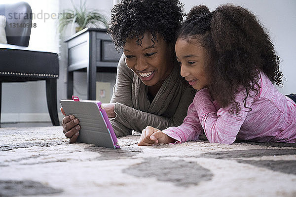 Glückliche Mutter und Tochter benutzen zu Hause einen Tablet-Computer auf dem Teppich