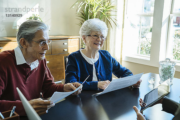 Älteres Ehepaar liest Dokumente  während es mit einem Finanzberater im Amt diskutiert