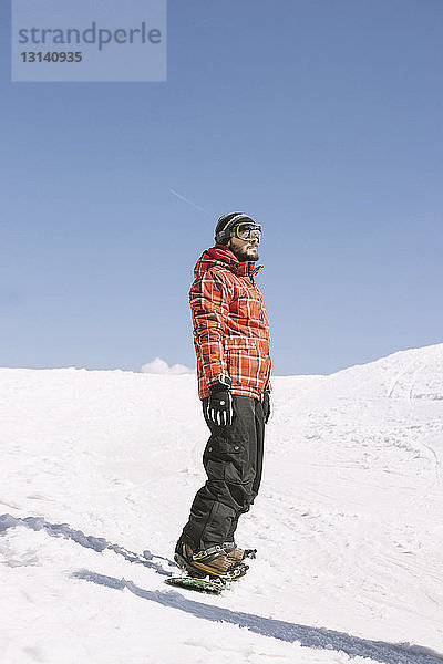 Mann schaut weg  während er im Winter auf dem Snowboard auf dem Feld steht
