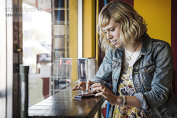 Frau benutzt Smartphone am Fenster im Cafe