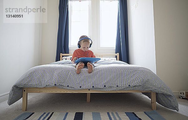 Junge hört Musik  während er zu Hause auf dem Bett sitzt