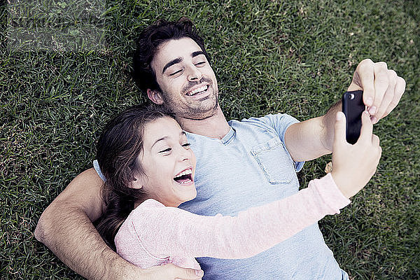 Glückliche Vater und Tochter  die im Gras liegend Selbsthilfe nehmen