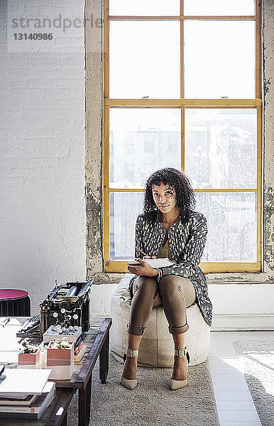 Porträt einer Geschäftsfrau  die in einem Buch schreibt  während sie im Kreativbüro sitzt