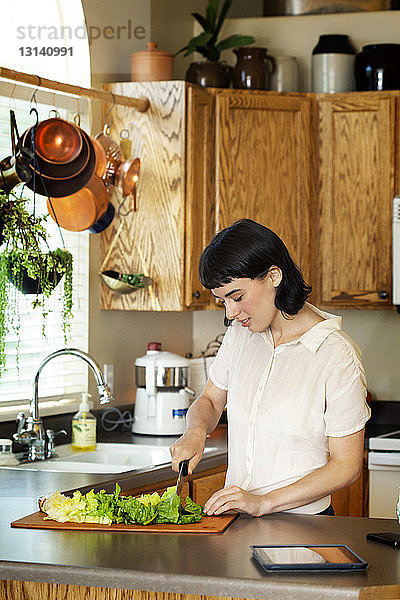 Lächelnde Frau schneidet frisches Gemüse  während sie zu Hause in der Küche steht