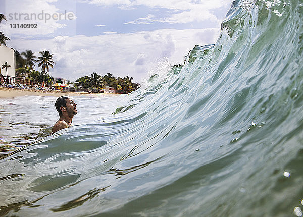 Seitenansicht eines Mannes  der die Meereswelle genießt  während er gegen den Himmel surft