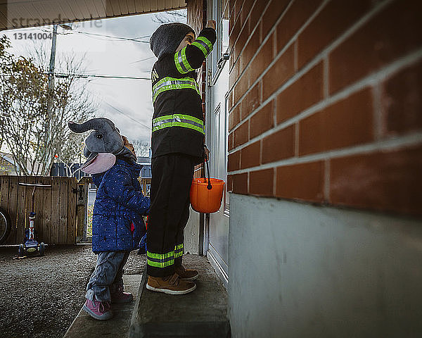 Seitenansicht von Geschwistern in Halloween-Kostümen  die auf Stufen am Haus stehen